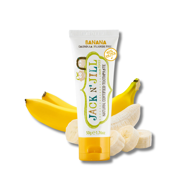 A tube of Jack N' Jill Banana Natural Certified Toothpaste is centered on a white background, surrounded by fresh yellow bananas and banana slices. The packaging is white with green and yellow accents, and the brand name 'JACK N' JILL' is clearly visible.