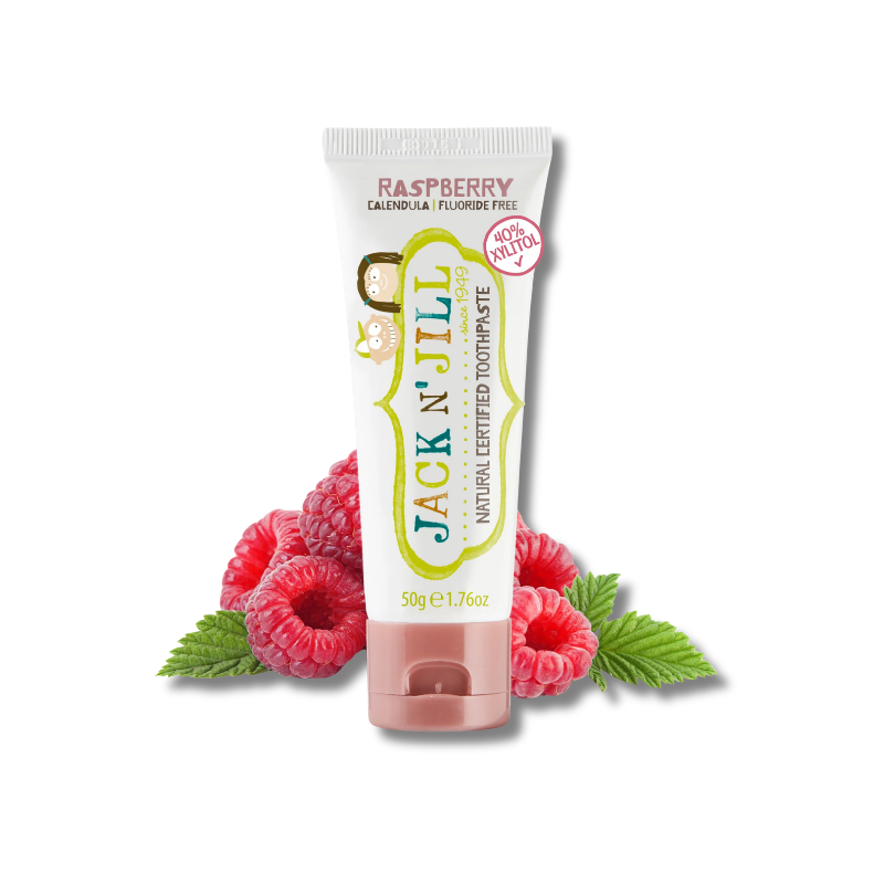 A tube of Jack N' Jill Raspberry toothpaste stands upright on a white background, styled with fresh red raspberries and green leaves at its base.