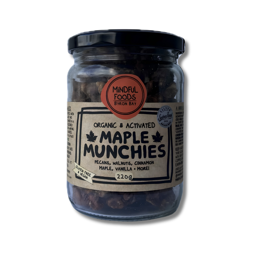 A glass jar of Mindful Foods 'Organic & Activated' Maple Munchies, featuring a black lid and a beige label with black text, set against a plain white background.