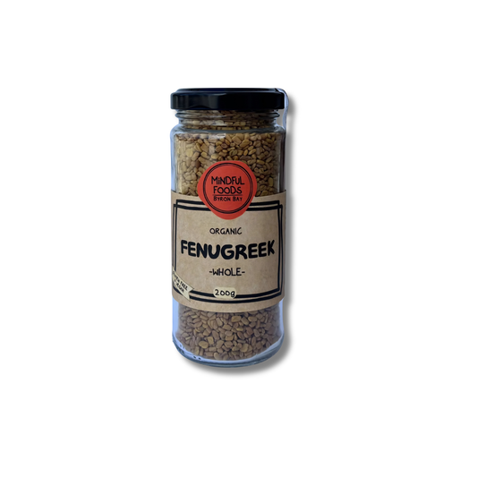 A glass jar of organic Fenugreek whole seeds with a black lid and a beige label, shown on a white background with a soft shadow.