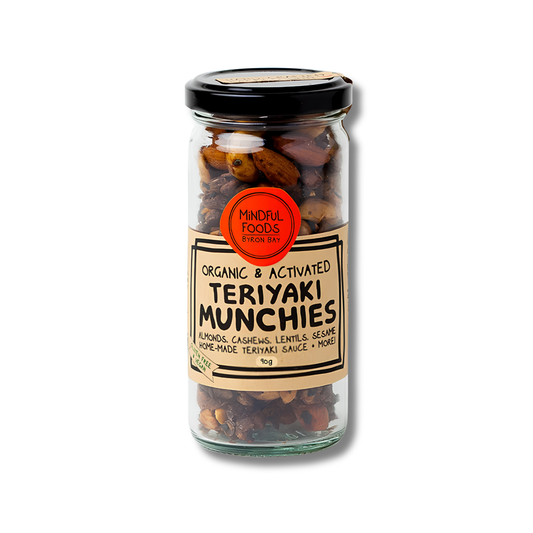 A glass jar of Mindful Foods Teriyaki Munchies on a white background. The jar contains a mixture of almonds, cashews, lentils, and seersalt, with a black lid and a beige label featuring a red circular logo.