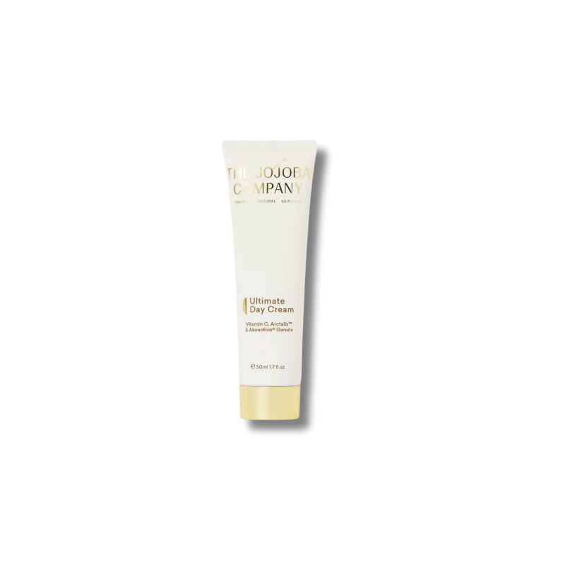 A single tube of The Jojoba Company Ultimate Day Cream on a clean white background. The tube is off-white with gold lettering and a gold cap, casting a soft shadow to the right.